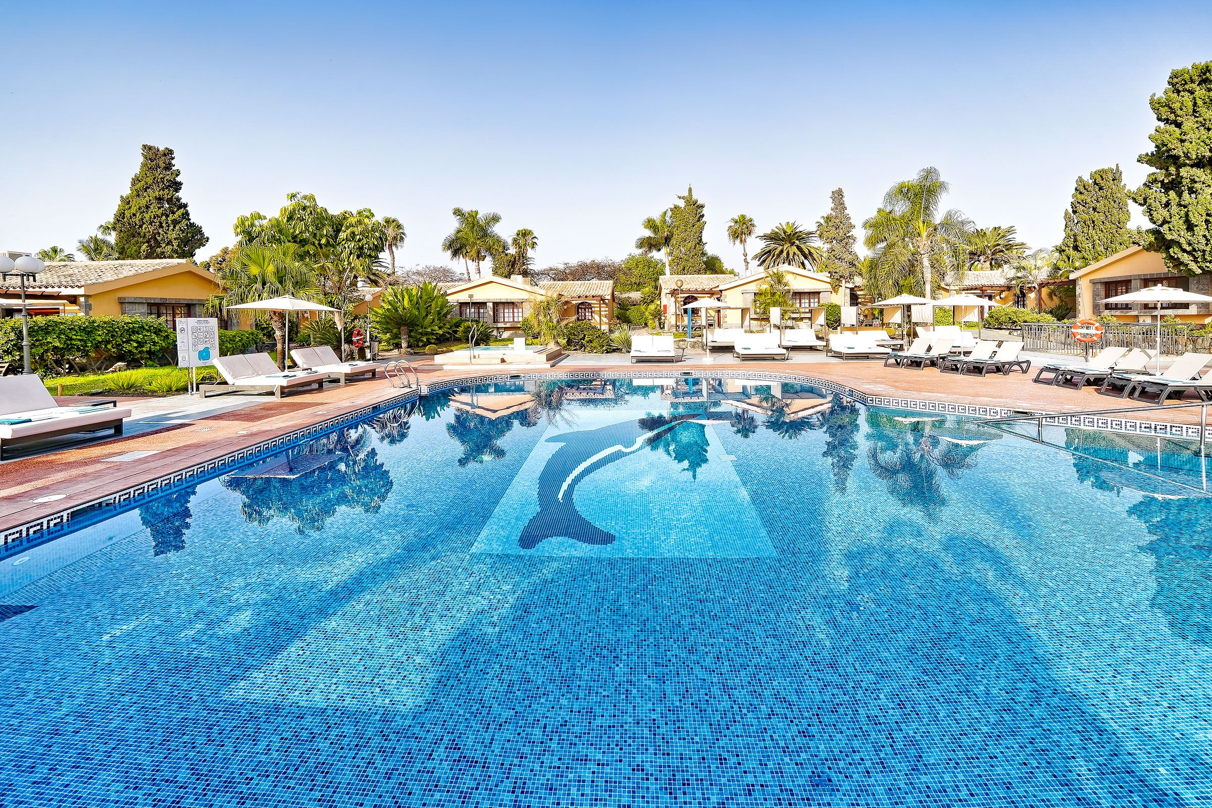 A swimming pool with lounge chairs, palm trees, and resort-style buildings.