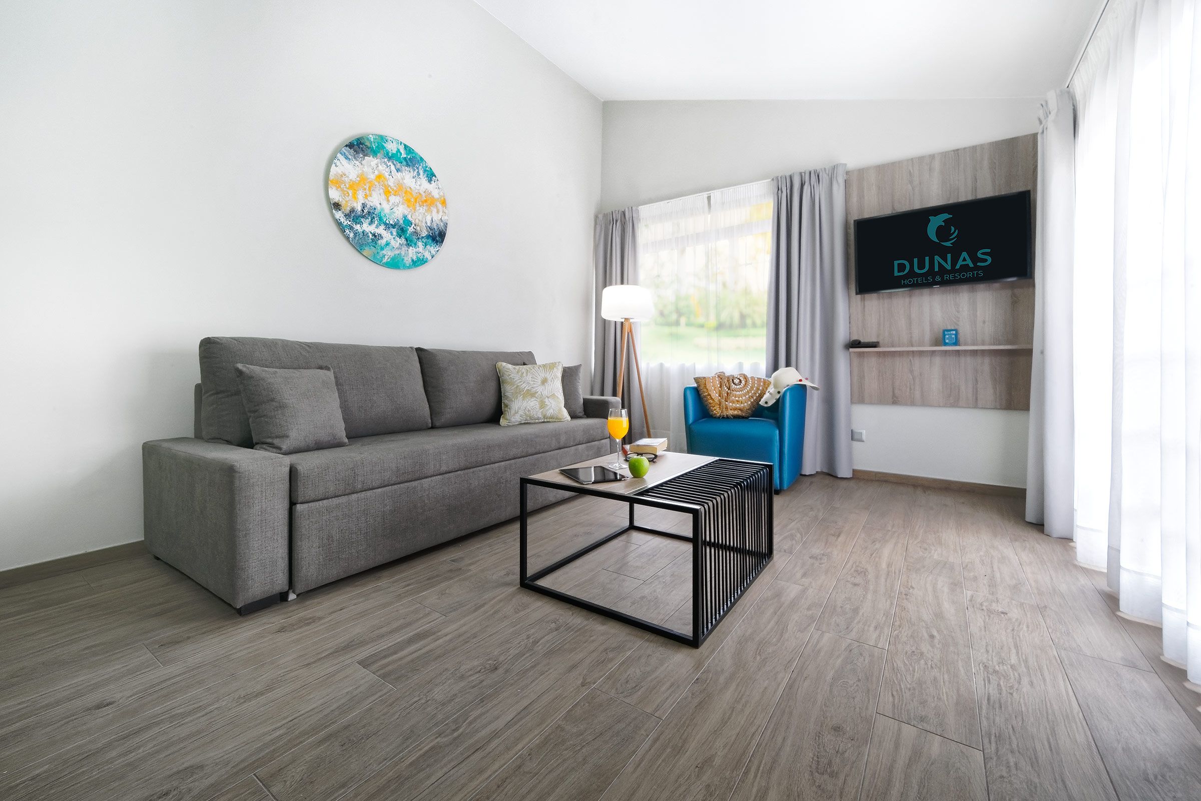 Een moderne woonkamer met een grijze bank, een salontafel, een televisie en een raam met gordijnen.