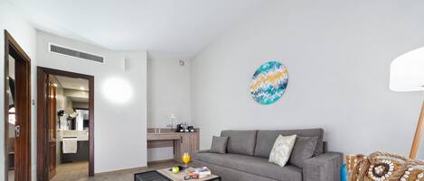 Un salón con un sofá gris, un sillón azul, una mesa de centro y una cocina al fondo.
