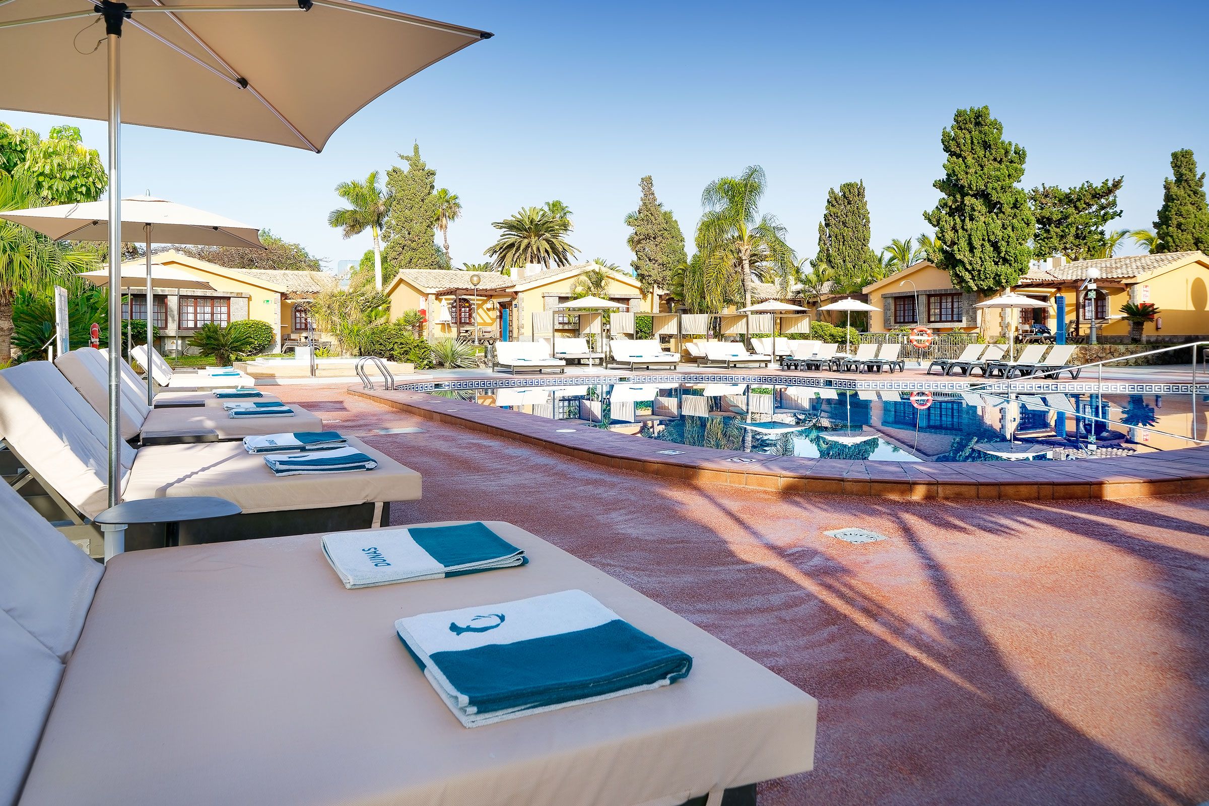 Un espace aménagé au bord de la piscine, avec des chaises longues et des transats, une piscine et un ciel dégagé.