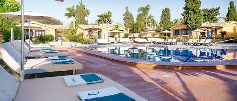 Zona junto a la piscina con sillones de descanso y tumbonas, una piscina y un cielo despejado.