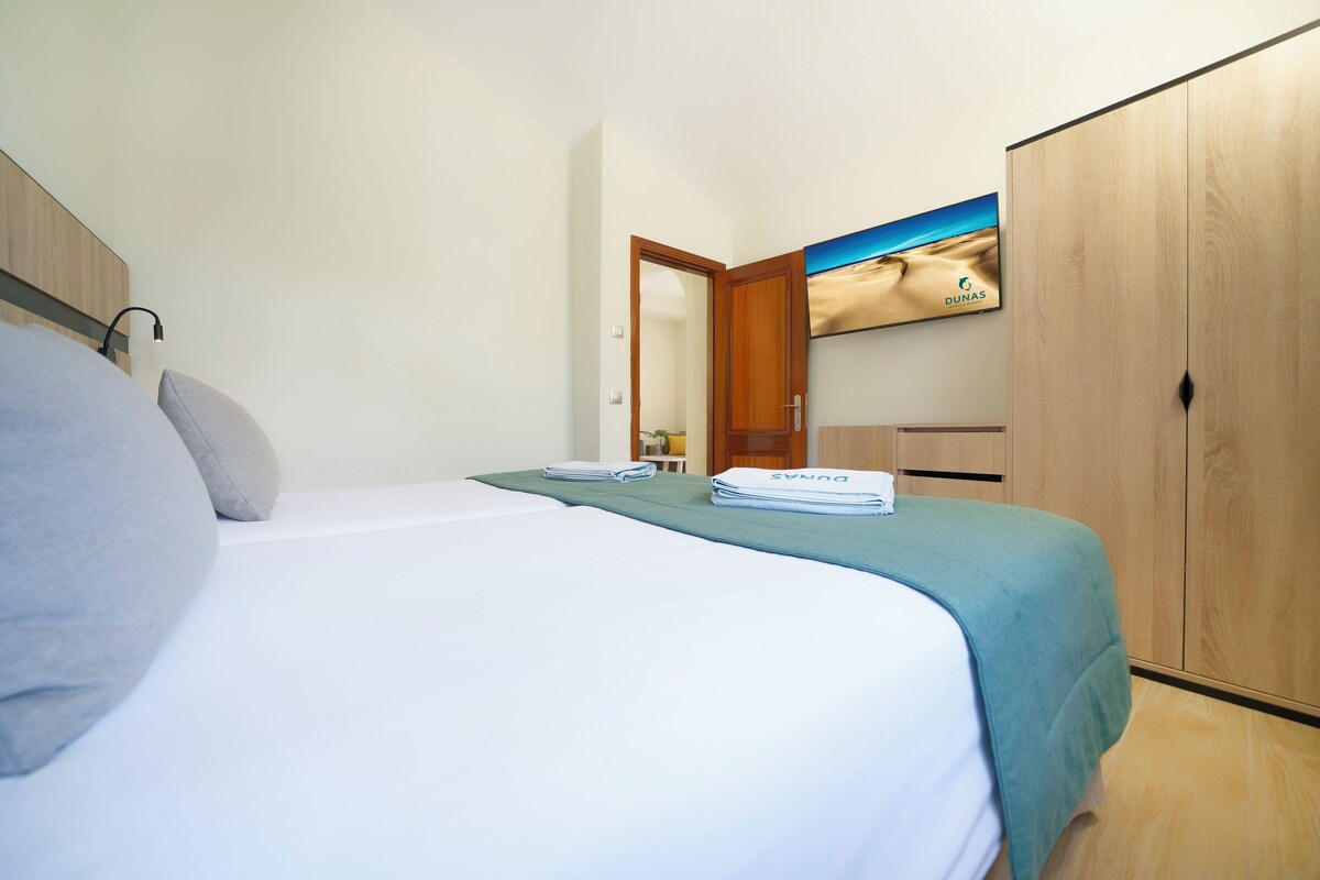 Quarto de hotel com cama, guarda-roupa, espelho e um quadro na parede.