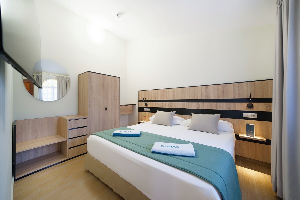 Quarto de hotel com cama, guarda-roupa, espelho e mesa de cabeceira.