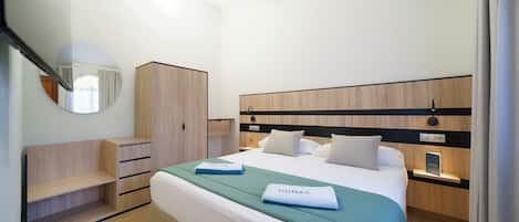 A hotel room with a bed, a wardrobe, a mirror, and a bedside table.