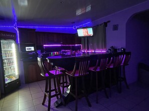A bar area with a long counter, bar stools, a television, and LED lighting. - Casa Club Bluaska (Las Horquetas)