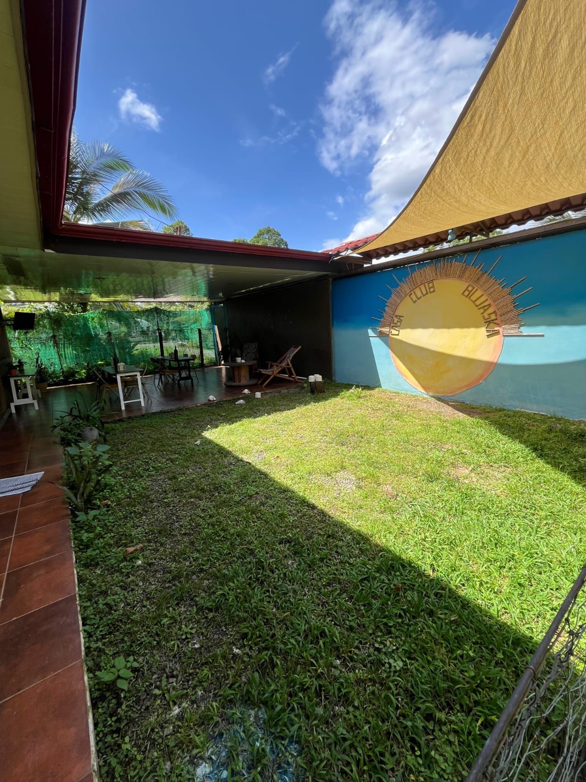Un espacio al aire libre techado con un mural, un césped y un patio con baldosas.