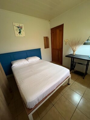 A bedroom with a bed, a desk, a chair, a door, and a wall-mounted lamp. - Casa Club Bluaska (Las Horquetas)