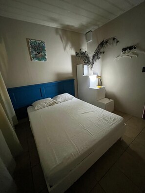 A bedroom with a bed, a nightstand, a wall-mounted lamp, a painting, and a decorative plant. - Casa Club Bluaska (Las Horquetas)