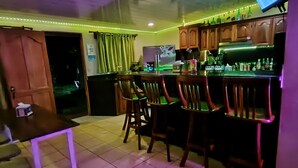 A bar area with wooden cabinets, a tiled floor, and a television mounted on the wall. - Casa Club Bluaska (Las Horquetas)