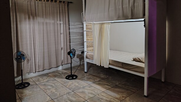 A room with a bunk bed, a standing fan, and a curtain. - Casa Club Bluaska (Las Horquetas)