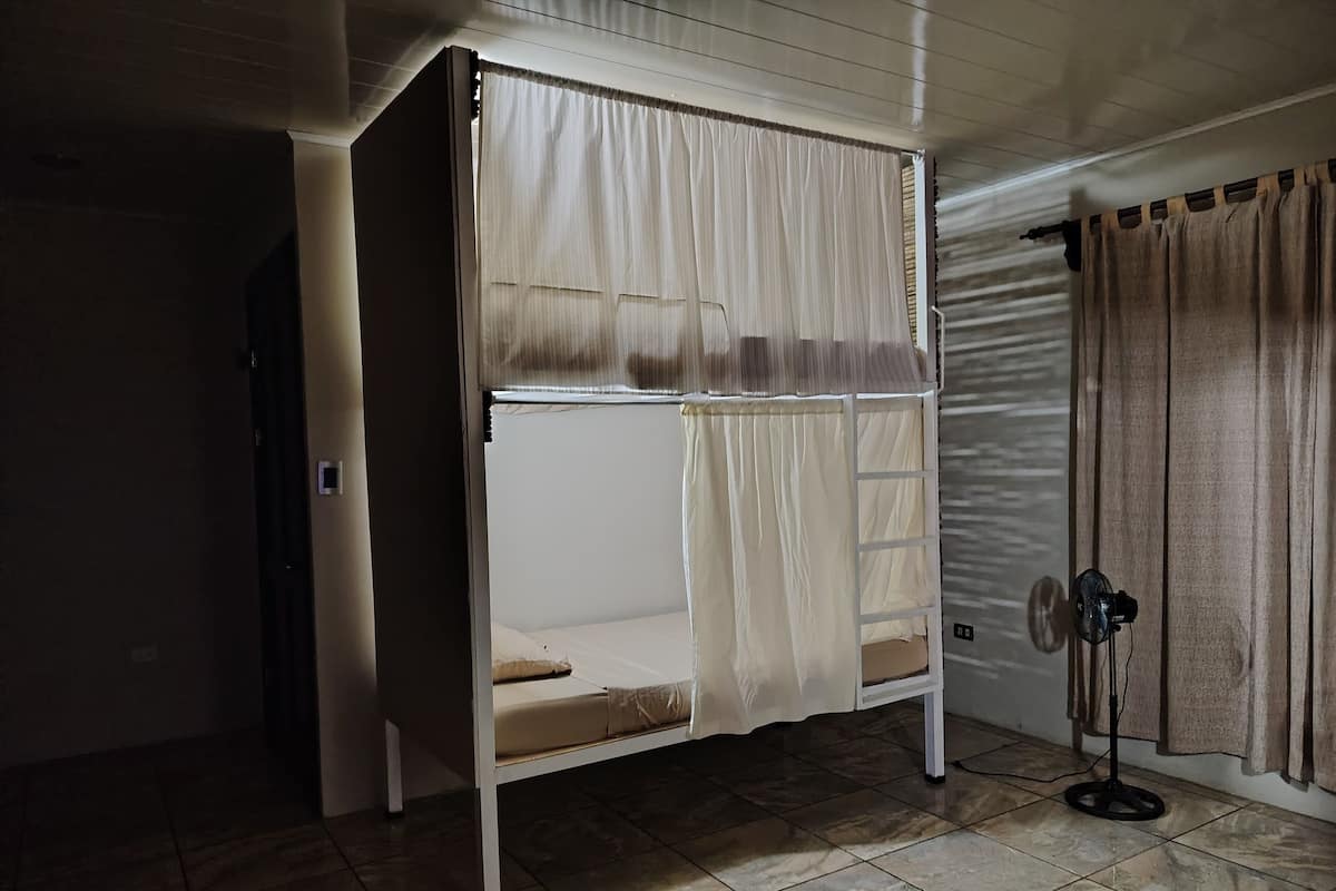 A bunk bed with a ladder, a power outlet, and a fan on the floor.