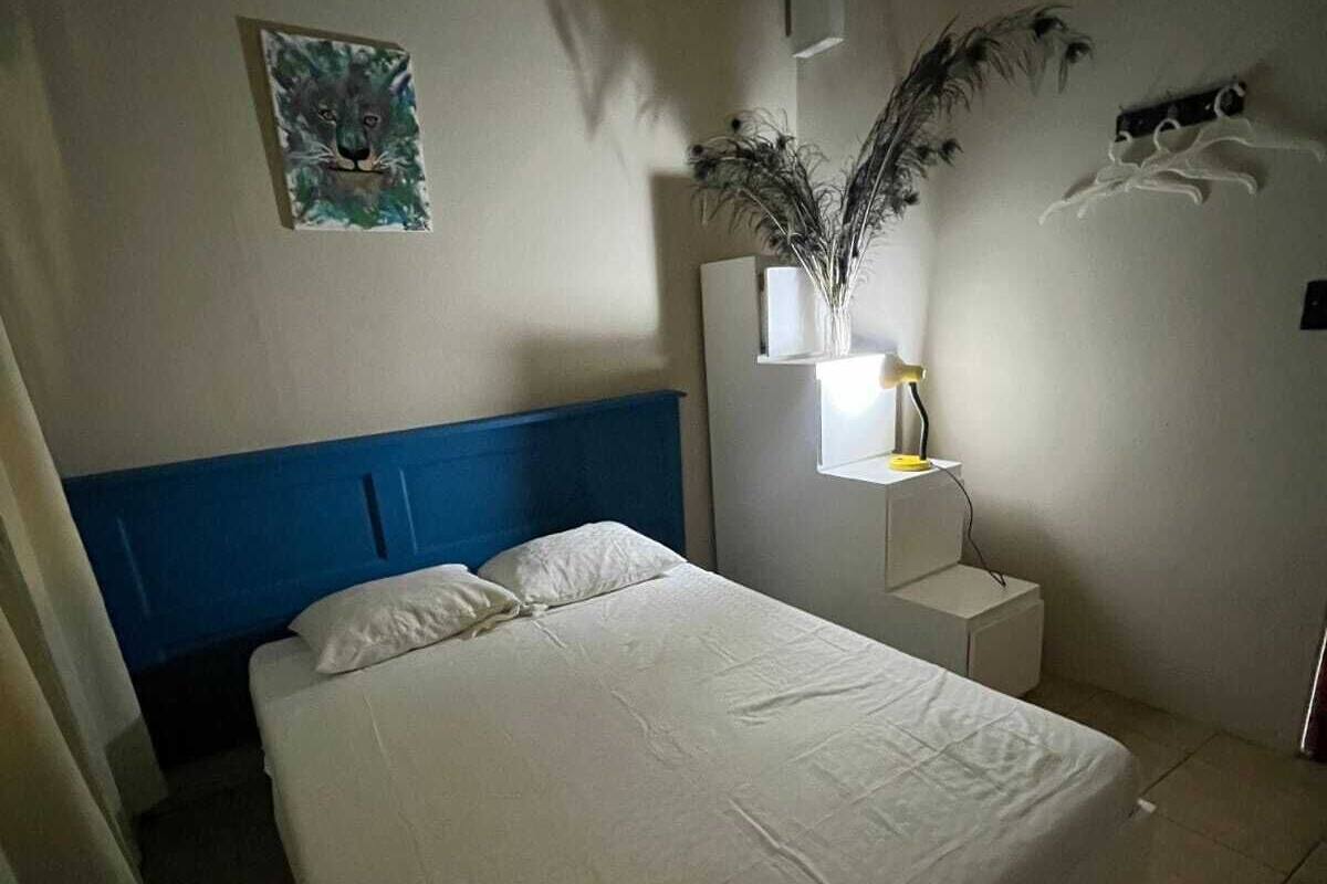 A bedroom with a bed, a nightstand, a wall-mounted lamp, a painting, and a decorative plant.