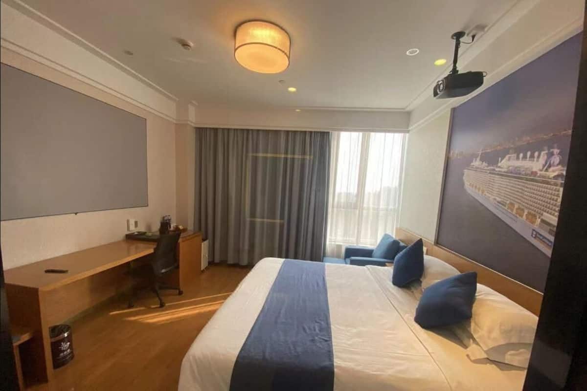 Habitación de hotel con una cama grande, un escritorio, una silla, un televisor y una ventana con cortinas.