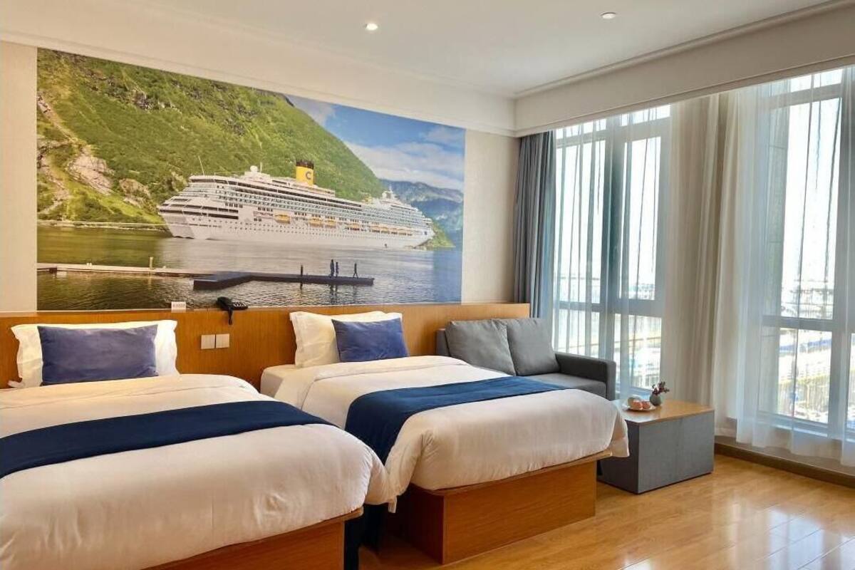 Habitación de hotel con dos camas, un ventanal con cortinas y un mural de un barco crucero.