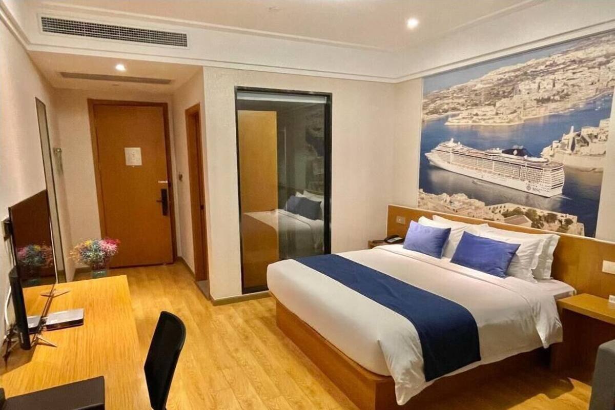 Habitación de hotel con cama, escritorio, silla, puerta corrediza y un cartel grande en la pared.