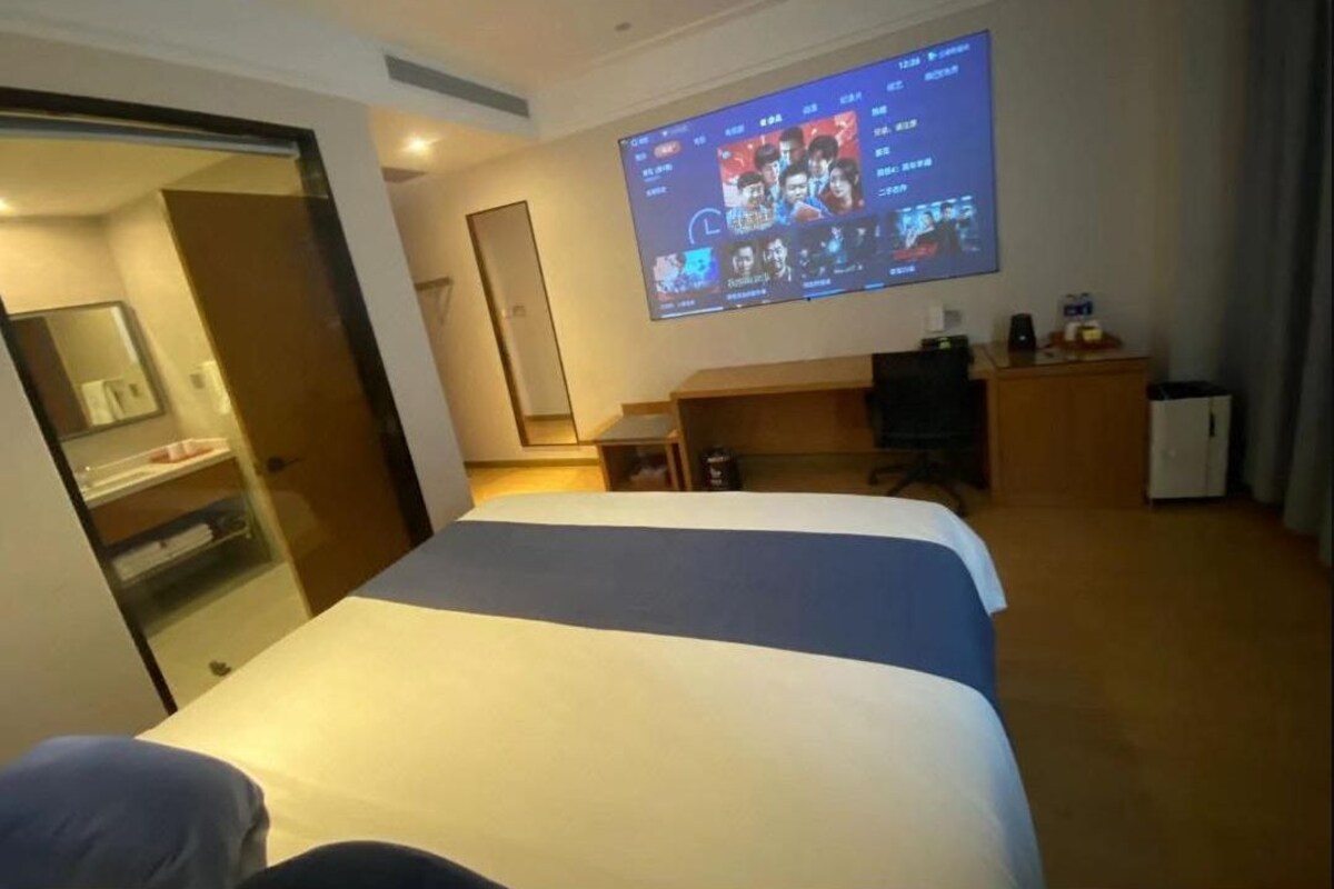 Una habitación de hotel con cama, escritorio, televisor montado en la pared y puerta que da a un baño.