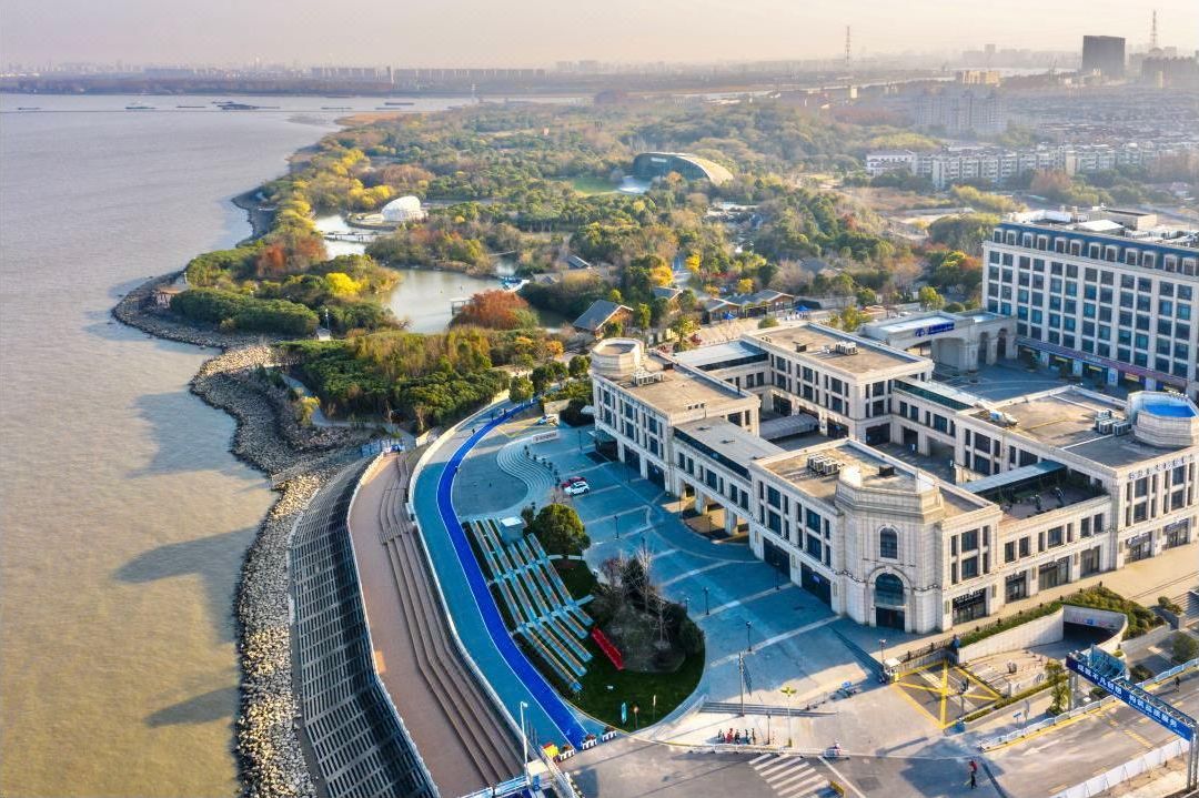 An aerial view of a waterfront property with a curved road, a large building with a dome, and a river.