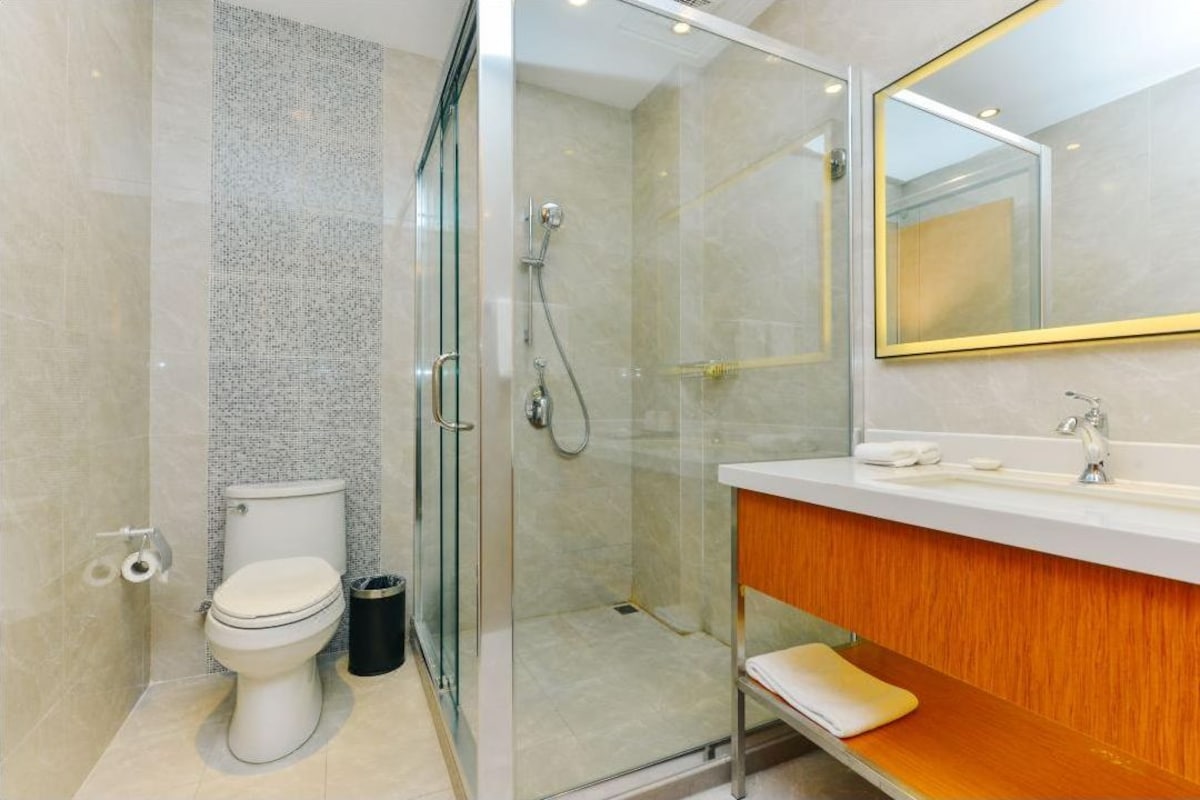 Une salle de bain moderne avec une douche à parois de verre, des toilettes blanches et un meuble-lavabo en bois doté d’un miroir.
