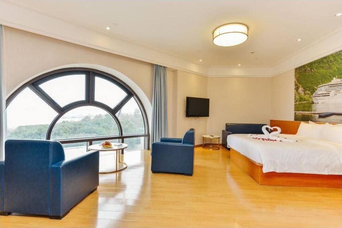Una habitación de hotel con un amplio ventanal de arco, una cama con ropa de cama blanca, un televisor de pantalla plana y una pequeña mesa redonda.