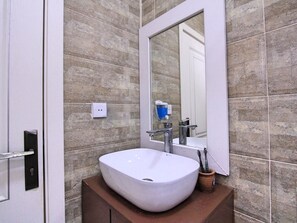Une salle de bain avec un lavabo blanc, un miroir et un mur recouvert de carreaux.