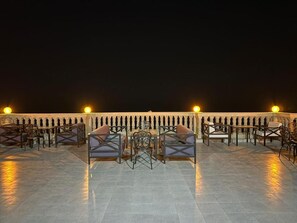 Un espace extérieur aménagé avec des tables et des chaises, un sol carrelé et une rambarde agrémentée de lumières.