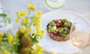 A plate of food with a glass of white wine and a glass of water on a table with a white tablecloth and yellow flowers. - Ikos Kissamos (Kissamos)