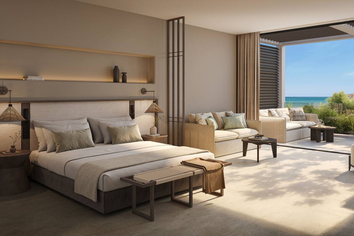 Un dormitorio moderno con una cama grande, un sofá, una mesita y vistas al océano.