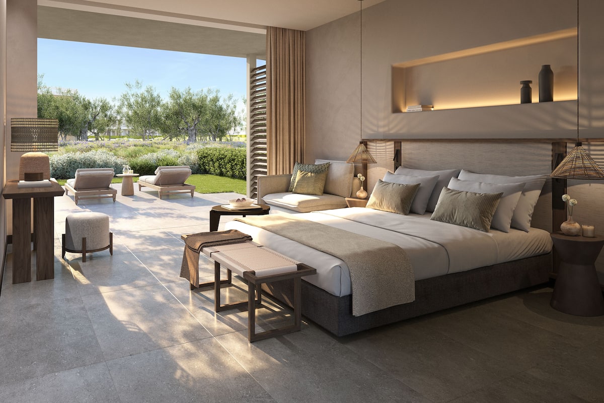 A modern bedroom with a large bed, a seating area with a sofa and chairs, and a view of a garden.