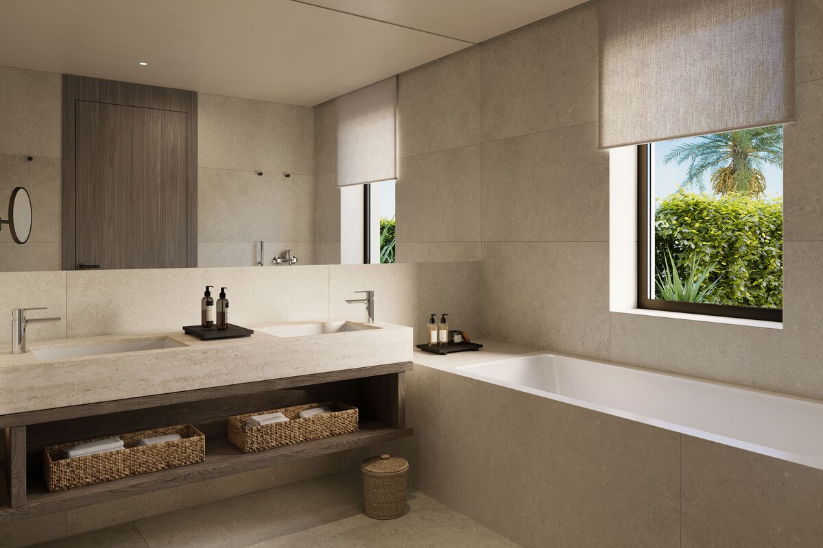 Un baño moderno con un espejo grande, dos lavamanos, una bañera y una ventana con vistas a la vegetación.