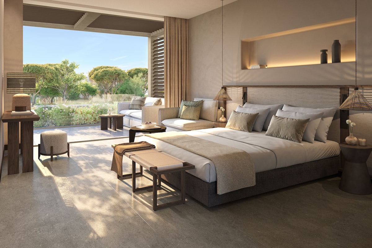 A modern bedroom with a large bed, a seating area, and a view of greenery.