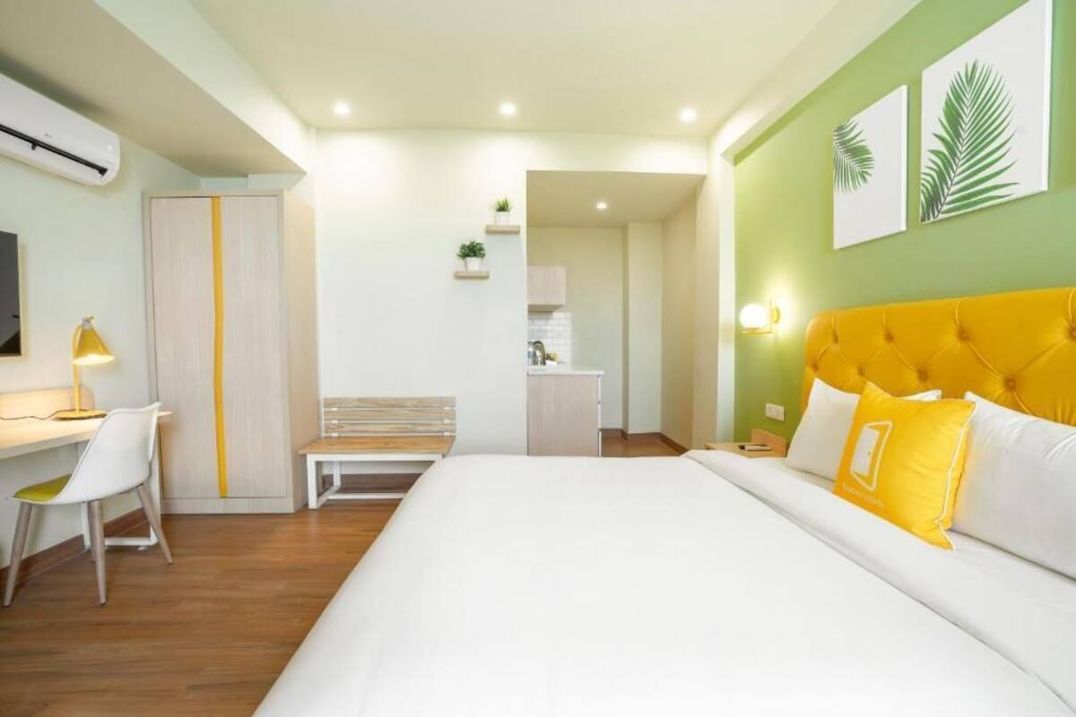 A hotel room with a bed, a desk, a chair, a bedside table, a lamp, a wardrobe, and a wall-mounted TV.