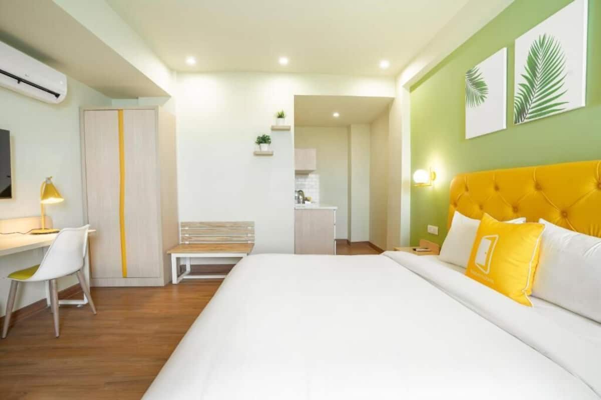 A hotel room with a bed, a desk, a chair, a bedside table, a lamp, a wardrobe, and a wall-mounted TV.