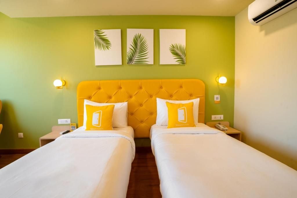 Habitación de hotel con dos camas, cabecera amarilla y cuadros colgados en la pared.