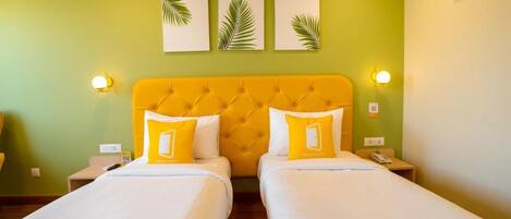 A hotel room with two beds, a yellow headboard, and wall-mounted artwork.
