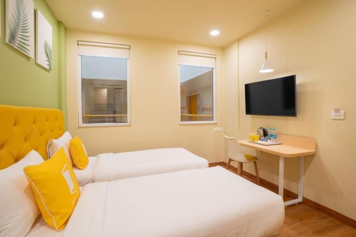 A hotel room with two beds, a desk, a TV, and a window.