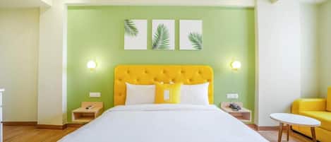 A hotel room with a large bed, a yellow headboard, green walls, and three leaf-patterned wall art pieces.