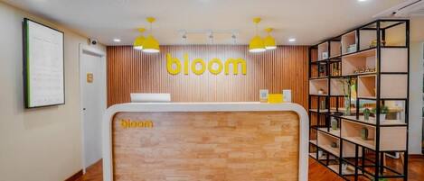 A reception desk with a 'bloom' sign, wooden paneling, and a plant shelf.