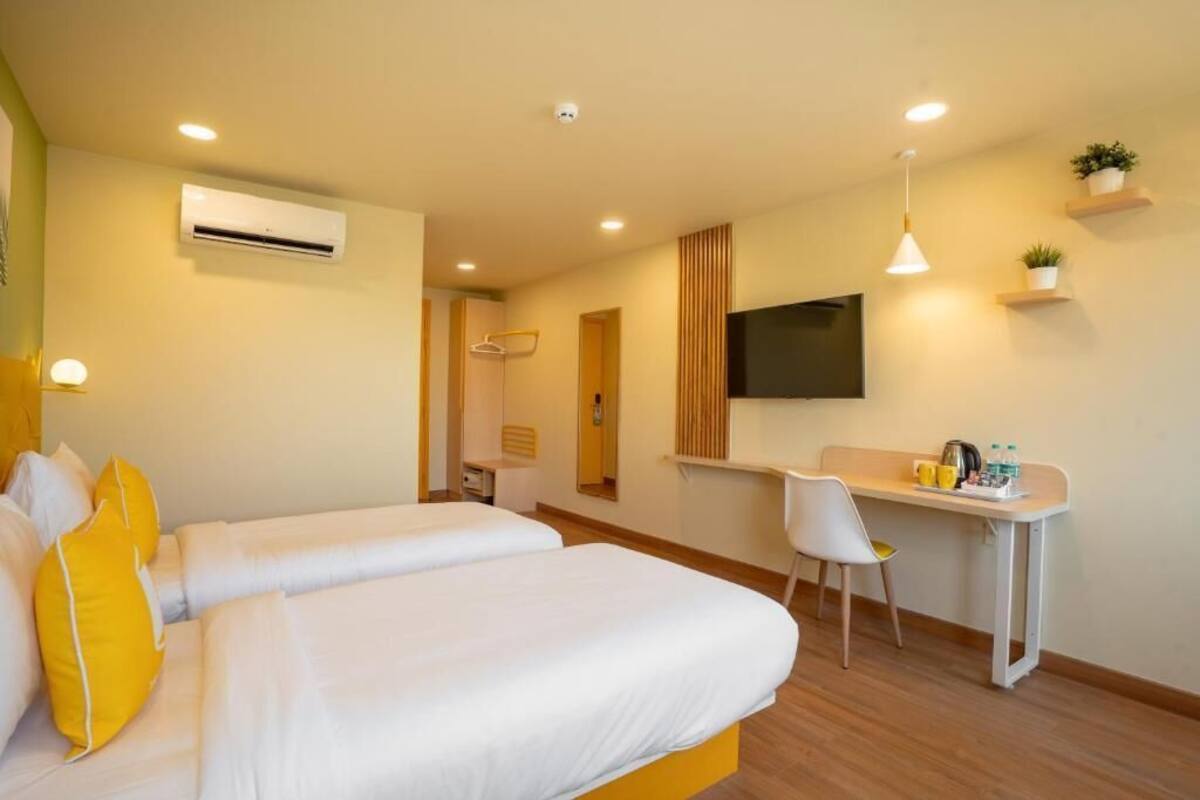 A hotel room with two beds, a desk, a chair, a TV, and a wall-mounted air conditioner.