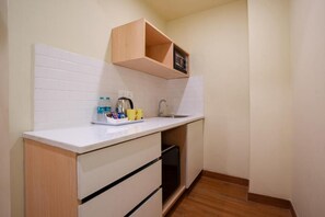A compact kitchen with white tiles, a wooden countertop, a sink, and a small shelf. - Bloom Hotel - Medicity Gurugram (Gurugram)