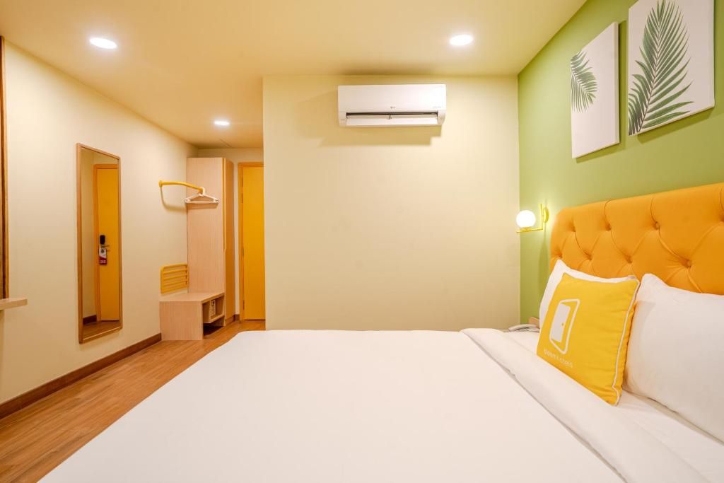 A hotel room with a bed, an air conditioning unit, a wardrobe, a mirror, and a wall-mounted lamp.