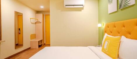 A hotel room with a bed, an air conditioning unit, a wardrobe, a mirror, and a wall-mounted lamp.