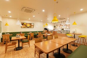 A restaurant with wooden tables and chairs, a green booth seating area, and yellow pendant lighting. - Bloom Hotel - Medicity Gurugram (Gurugram)