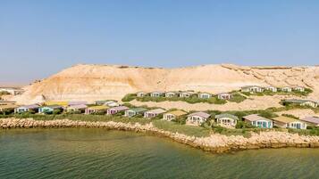A coastal resort with villas along a rocky shoreline, clear skies, and a large cliff in the background.