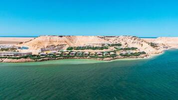 An aerial view of a coastal resort with multiple buildings, a sandy beach, and clear turquoise waters.
