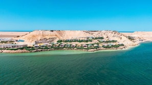 Vista aerea di una località balneare con numerosi edifici, una spiaggia sabbiosa e acque cristalline color turchese.