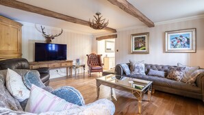 A living room with a television, leather sofas, a glass coffee table, wooden beams, and framed artwork on the walls.