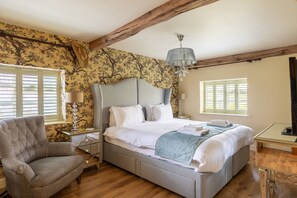 A bedroom with a bed, a chair, a nightstand, a lamp, and a chandelier.