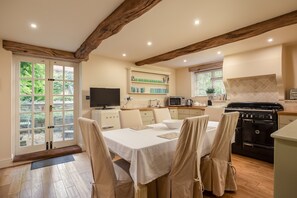 Un comedor con mesa, sillas, televisor y cocina equipada con estufa y microondas.