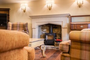 A cozy living room with a fireplace, plaid furniture, and wall sconces.