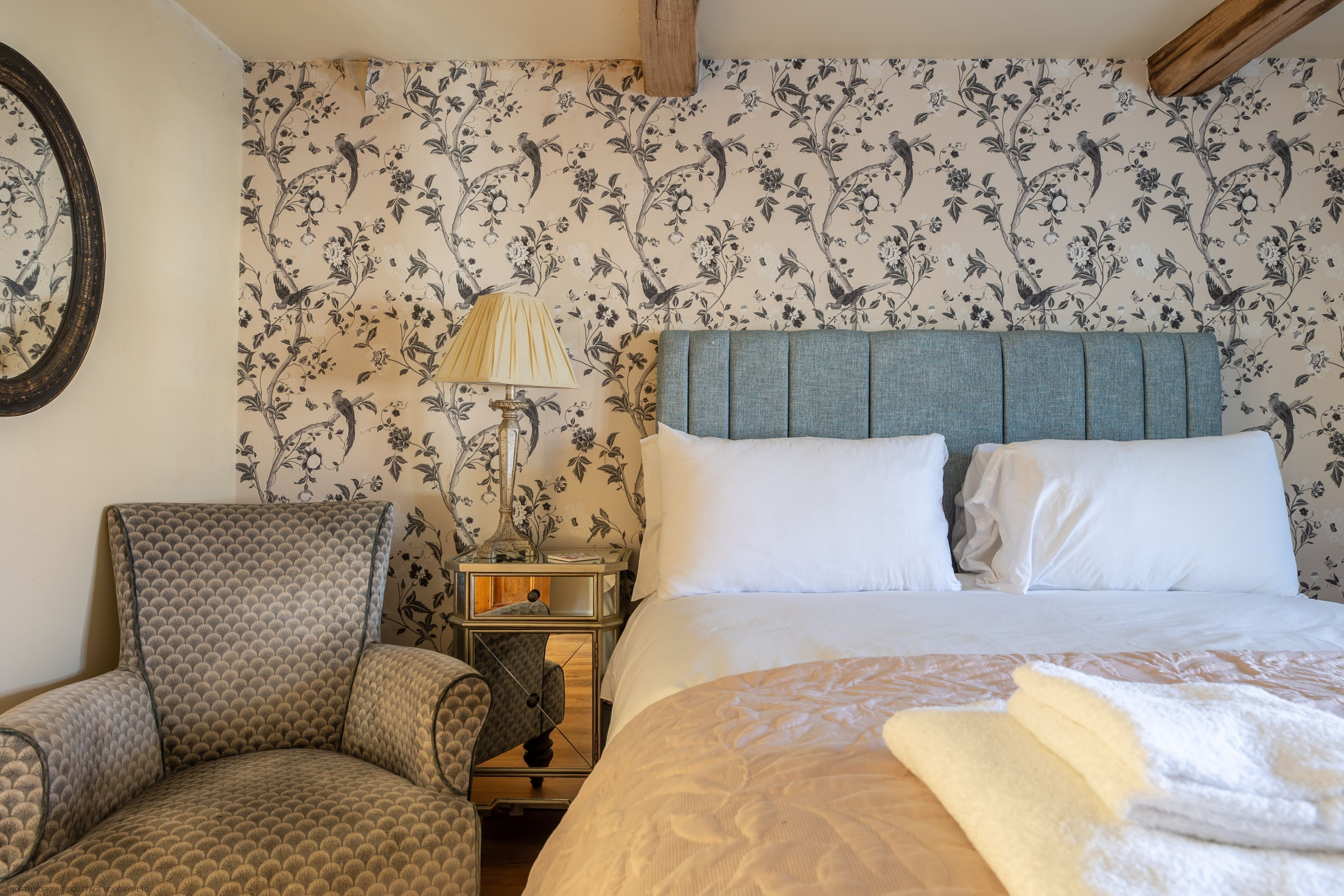 A bedroom with a bed, a chair, a nightstand, and a mirror.